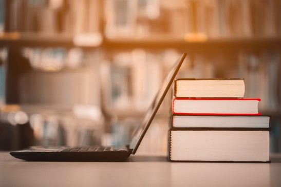 Ausbildung bei EWE Auf einem Tisch befinden sich ein Laptop. Dahinter liegt ein Stapel mit 4 Büchern. Im Hintergrund ein großes Bücherregal, mit vielen Büchern.
